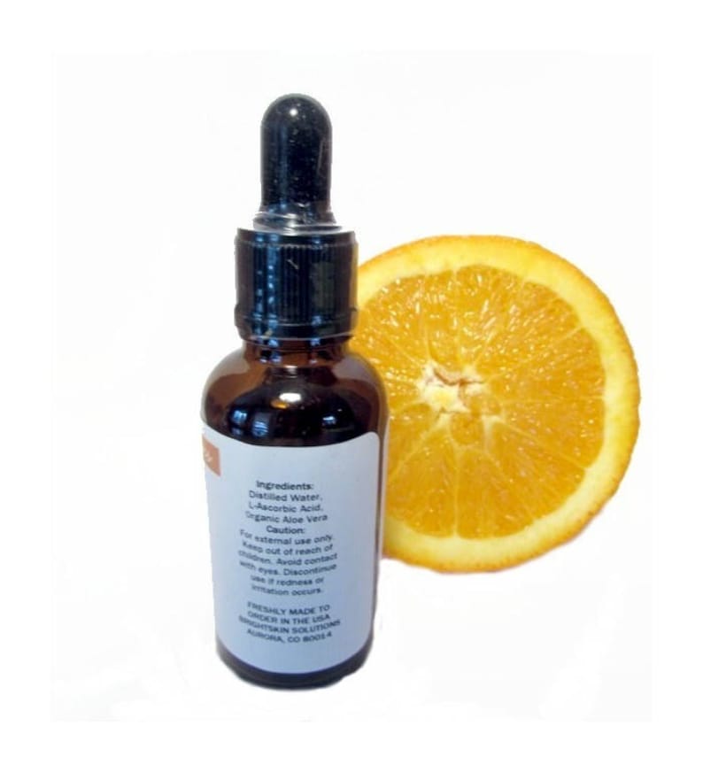 Puede incluir: Una botella de vidrio marr&oacute;n con un cuentagotas negro y una etiqueta blanca, junto a una rodaja de naranja. La etiqueta enumera ingredientes como agua destilada y &aacute;cido L-asc&oacute;rbico. La botella es solo para uso externo.