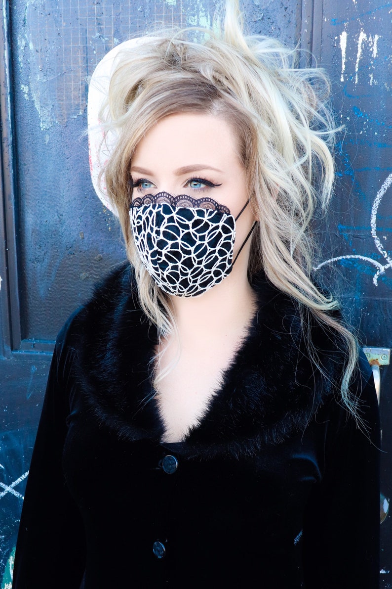 Może przedstawiać: Kobieta z blond włosami w czarnej aksamitnej kurtce z kołnierzem z futra i czarno-białą maską na twarz.