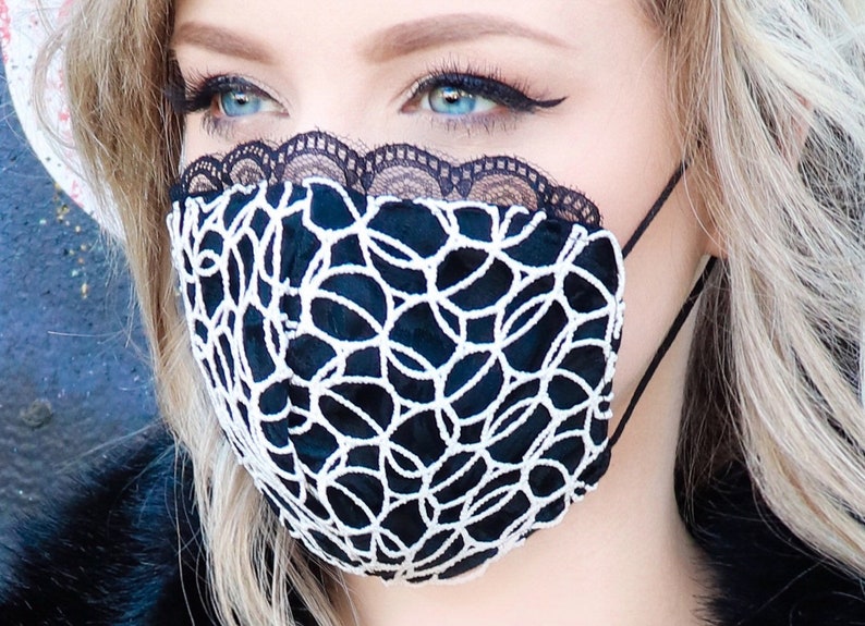 Może przedstawiać: Czarna maska ​​na twarz z białymi koronkami. Maska ​​ma geometryczny wz&oacute;r i jest wykonana z miękkiej, oddychającej tkaniny.