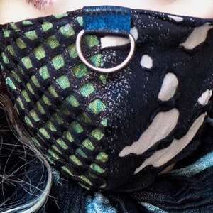 May include: A black and green face mask with a white and black patterned design. The mask has a blue strap with a silver ring.