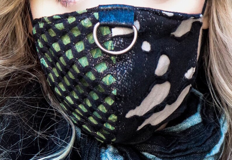 May include: A black and green face mask with a white and black patterned design. The mask has a blue strap with a silver ring.