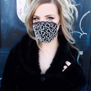 Może przedstawiać: Kobieta w czarnej aksamitnej kurtce z kołnierzem z futra i czarno-białą koronkową maską na twarz.