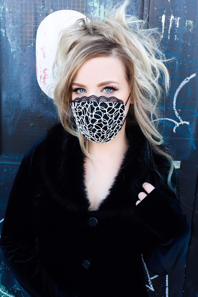 Może przedstawiać: Kobieta w czarnej aksamitnej kurtce z kołnierzem z futra i czarno-białą koronkową maską na twarz.