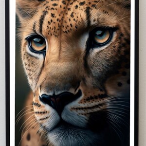 May include: Framed print showing a close-up of a cheetah's face. The cheetah has a tan coat with black spots and striking blue-yellow eyes. The image is framed in a black border, creating a dramatic effect.
