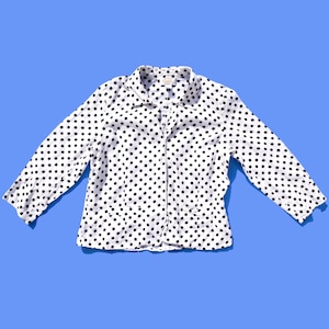 Puede incluir: Una camisa blanca de botones con lunares negros. La camisa tiene mangas largas y cuello.