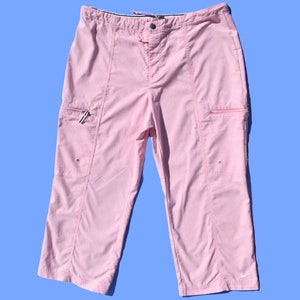 May include: Pink capri pants with two zippered pockets on the sides and a Nike logo on the bottom right leg.