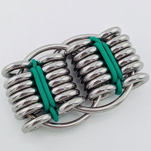 May include: A silver metal ring with green rubber bands woven through it. The ring is made of multiple interlocking circles.