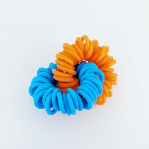 May include: Two coiled hair ties, one blue and one orange, are intertwined together.