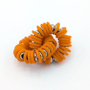 Peut inclure: Trois élastiques à cheveux orange enroulés avec des perles argentées. Les élastiques à cheveux sont entrelacés.