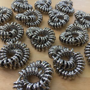 Puede incluir: Una colecci&oacute;n de anillos met&aacute;licos plateados y brillantes dispuestos en espiral. Los anillos est&aacute;n enrollados con fuerza, creando una forma circular. Los objetos est&aacute;n sobre una superficie de madera marr&oacute;n claro.