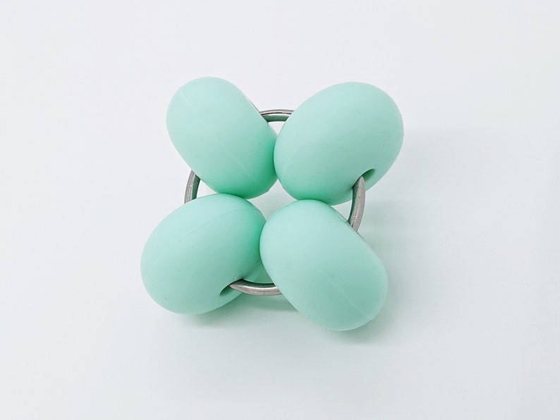Puede incluir: Cuatro cuentas de silicona verde menta est&aacute;n conectadas por un anillo de metal plateado. Las cuentas son redondas y lisas.