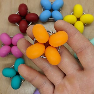 Puede incluir: Un conjunto de seis juguetes sensoriales de diferentes colores, incluyendo naranja, amarillo, azul, rosa, turquesa y morado. Cada juguete es una esfera con un peque&ntilde;o agujero en el centro, lo que permite conectarlo a otros juguetes. Los juguetes est&aacute;n dispuestos en forma de estrella.