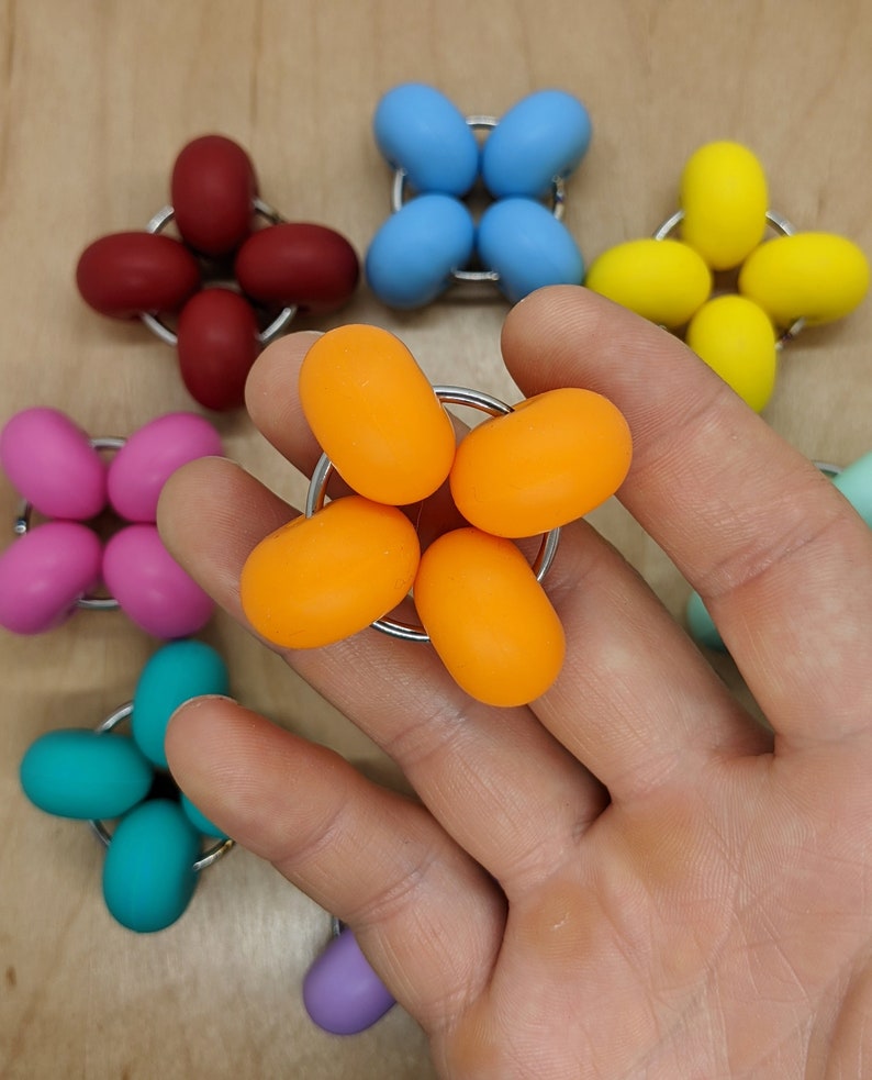 Puede incluir: Un conjunto de seis juguetes sensoriales de diferentes colores, incluyendo naranja, amarillo, azul, rosa, turquesa y morado. Cada juguete es una esfera con un peque&ntilde;o agujero en el centro, lo que permite conectarlo a otros juguetes. Los juguetes est&aacute;n dispuestos en forma de estrella.