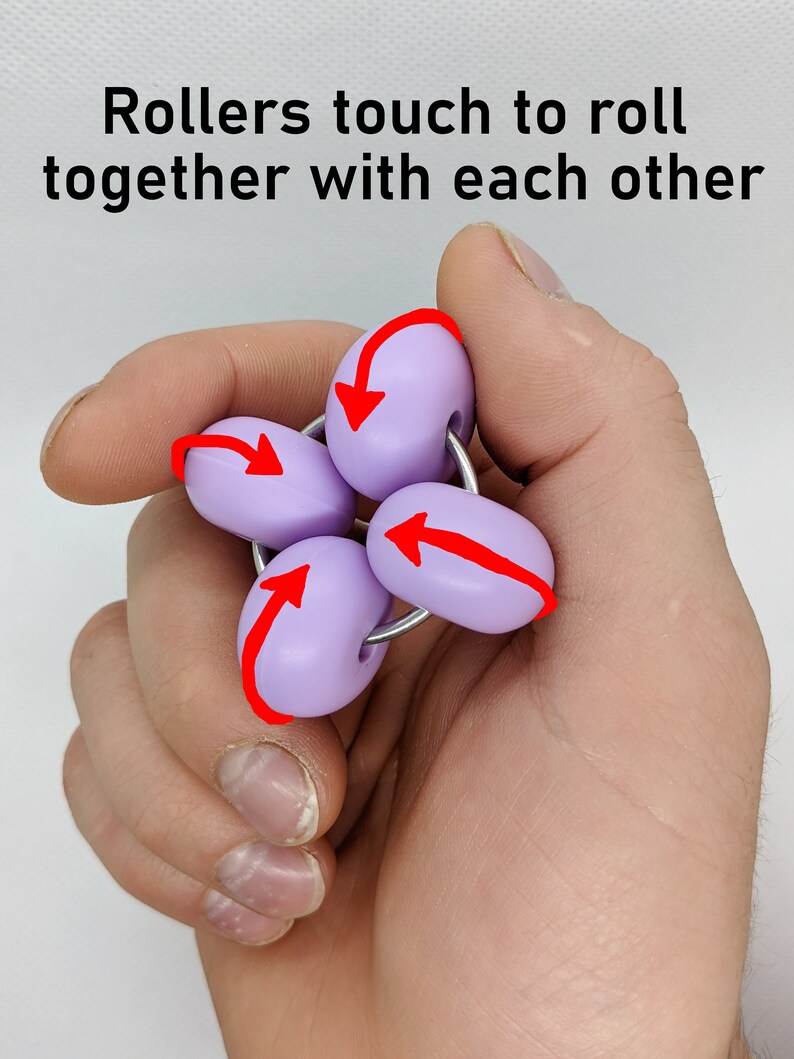 Puede incluir: Un juguete antiestr&eacute;s morado con cuatro rodillos que giran alrededor de un anillo de metal. Los rodillos est&aacute;n conectados al anillo y se tocan entre s&iacute;. El juguete se sostiene en una mano, y las flechas indican la direcci&oacute;n en la que los rodillos pueden girar.