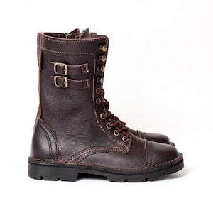 May include: Brown leather combat boots with a lace-up front and two buckles on the side. The boots have a thick rubber sole.