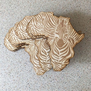 May include: A set of wooden coasters shaped like the continent of Africa, with a zebra pattern.