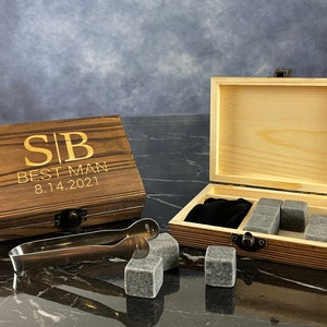 May include: A wooden box with a hinged lid, engraved with the initials "SB" and the text "Best Man 8.14.2021". The box contains a set of gray whiskey stones and a pair of silver tongs.