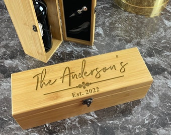 May include: A wooden box with a personalized inscription "The Anderson's Est. 2022" and a latch. The box is open, revealing a bottle of wine and a set of wine accessories.