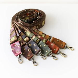 May include: A set of six camera straps with different colored leather and metal clasps. The straps are made of brown fabric with a floral pattern and have a green and gold trim.