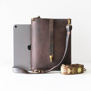 May include: A brown leather tablet sleeve with a brass clasp and adjustable strap. The sleeve is shown next to a tablet and a brown and gold patterned strap.