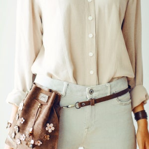Peut inclure: Une banane en daim marron avec des fleurs roses et marrons. La banane est port&eacute;e sur une chemise boutonn&eacute;e marron clair et un jean gris clair.