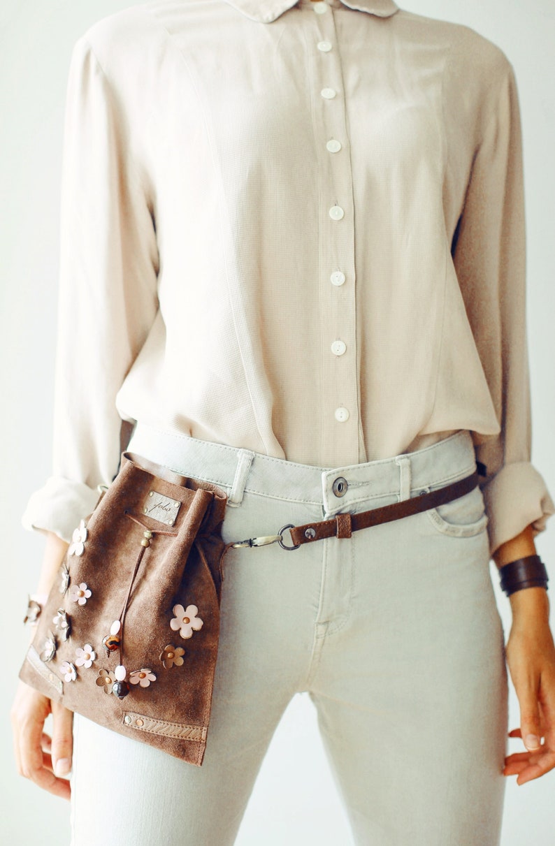 Peut inclure: Une banane en daim marron avec des fleurs roses et marrons. La banane est port&eacute;e sur une chemise boutonn&eacute;e marron clair et un jean gris clair.