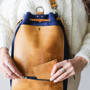 May include: A blue and brown leather drawstring backpack with a zippered pocket and a small leather wallet inside the pocket.