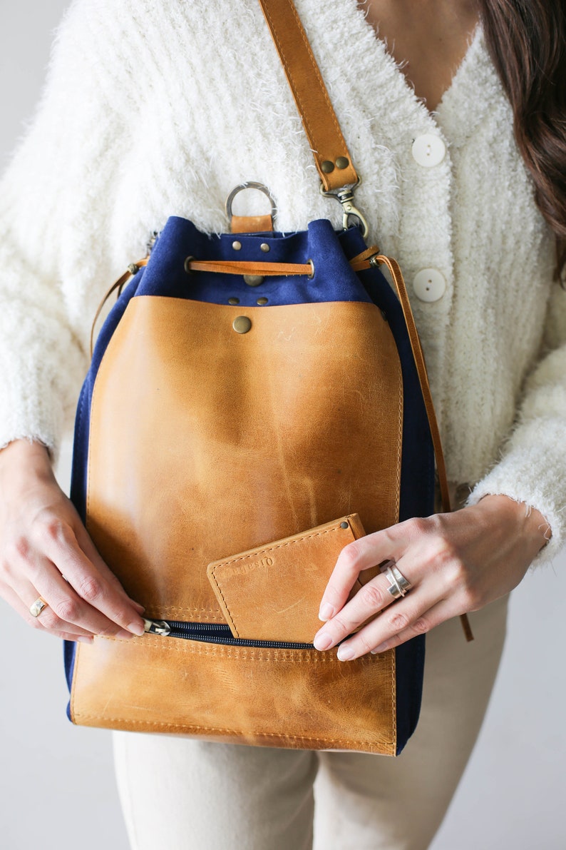 May include: A blue and brown leather drawstring backpack with a zippered pocket and a small leather wallet inside the pocket.