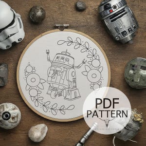 Könnte beinhalten: Eine Schwarzweiß-Zeichnung eines Roboters mit floralen Akzenten auf weißem Hintergrund. Das Bild befindet sich in einem runden Stickrahmen. Der Text "PDF PATTERN" befindet sich unter dem Rahmen.