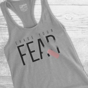 May include: Gray racerback tank top with the words "ERASE YOUR FEAR" printed in black. A pink eraser graphic is partially covering the word "FEAR". The tank top is made of a soft material.