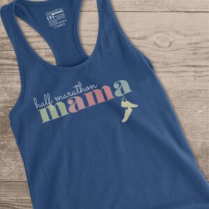 May include: A blue racerback tank top with the words "half marathon mama" in a colorful, stylized font. The word "mama" is in pink, green, and blue. A pair of running shoes is printed next to the word "mama".
