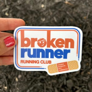 May include: A rectangular sticker with the words "broken runner" in orange and blue, with "running club" below. A bandage graphic reads "Turning setbacks into comebacks!" The sticker has a white background with a blue and red border.
