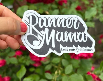 May include: A white sticker with the words "Runner Mama" in a stylized font, with the text "Long runs & little ones" below. The sticker is held in front of a background of red roses and green leaves.