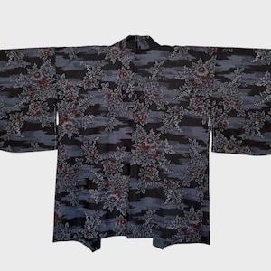 Puede incluir: Un kimono azul oscuro con un estampado floral. El kimono presenta un diseño repetido de flores y hojas en tonos grises y rojos sobre un fondo de rayas horizontales. Las mangas son anchas y la prenda está plana.