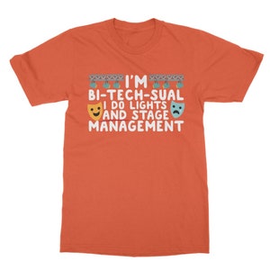Op de afbeelding: Oranje T-shirt met de tekst "I'm Bi-Tech-Sual I do lights and stage management" met twee emoji-gezichten aan weerszijden van de tekst.