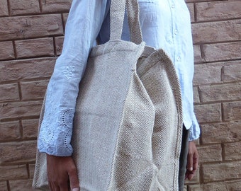 Könnte beinhalten: Eine große, beige Tragetasche mit Fischgrätenmuster. Die Tasche hat stabile Griffe und wird von einer Person getragen, die ein hellblaues Hemd und eine graue Hose trägt. Das Design der Tasche ist schlicht und funktional.