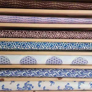 May include: A collection of patterned paper rolls in a wooden shelf. The rolls display various designs, including dots, geometric shapes, and floral patterns. Colors include brown, blue, and white. The paper rolls are neatly organized and ready for use.
