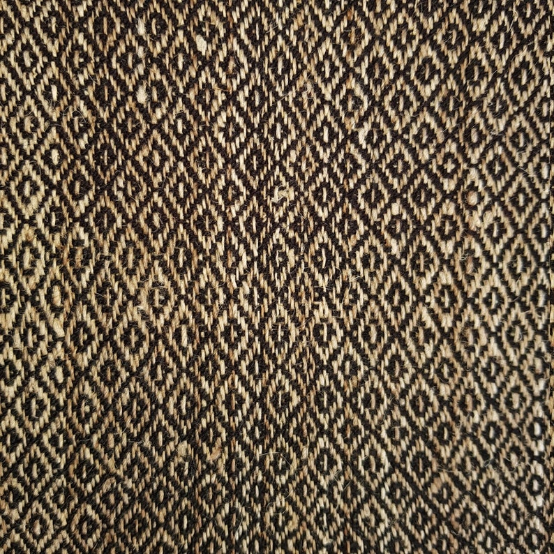 May include: Close-up of a woven textile with a repeating diamond pattern. The fabric features a natural beige and dark brown color scheme, creating a textured, geometric design. The weave appears to be tightly constructed, suggesting durability.