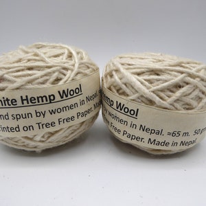 Peut inclure: Deux pelotes de fil de laine de chanvre blanc. Chaque pelote porte une &eacute;tiquette indiquant "White Hemp Wool" et "Hand spun by women in Nepal." Le fil mesure environ 65 m&egrave;tres et p&egrave;se 50 grammes.