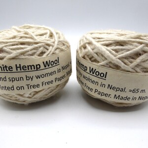 Peut inclure: Deux pelotes de fil de laine de chanvre blanc. Chaque pelote est envelopp&eacute;e d'une &eacute;tiquette indiquant "White Hemp Wool" et "Hand spun by women in Nepal". Le fil est de couleur blanc cass&eacute; naturel. L'&eacute;tiquette indique &eacute;galement la longueur approximative du fil, environ 65 m.