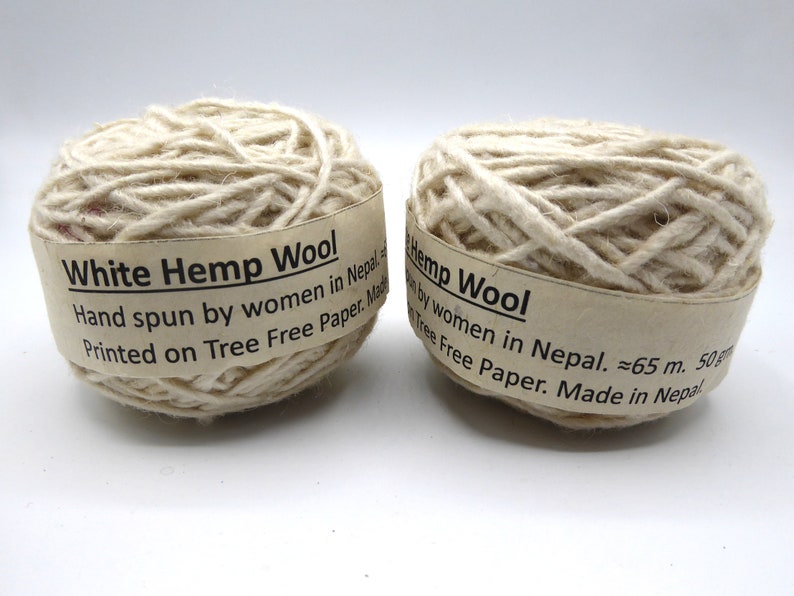 Peut inclure: Deux pelotes de fil de laine de chanvre blanc. Chaque pelote est envelopp&eacute;e d'une &eacute;tiquette indiquant "White Hemp Wool" et "Hand spun by women in Nepal". Le fil est de couleur blanc cass&eacute; naturel. L'&eacute;tiquette indique &eacute;galement la longueur approximative du fil, environ 65 m.