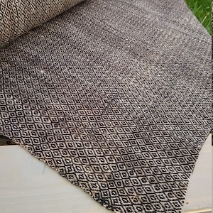 May include: A rolled-up, brown and cream-colored rug with a repeating diamond pattern. The rug is made of a woven material and has a textured appearance. The diamond pattern is a classic design element.