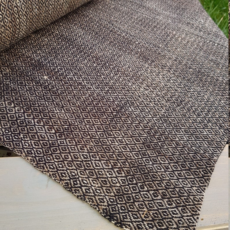 May include: A rolled-up, brown and cream-colored rug with a repeating diamond pattern. The rug is made of a woven material and has a textured appearance. The diamond pattern is a classic design element.