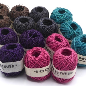 May include: A selection of hemp twine balls in shades of brown, black, teal, purple, and pink. Each ball is labelled with "HEMP" and "100% HAND MADE IN NEPAL". The twine is tightly wound and appears to be of natural fibre. Ideal for crafting and various projects.