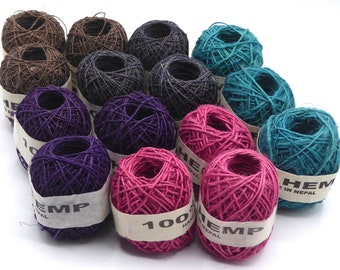 May include: A collection of hemp twine balls in various colors, including brown, black, teal, purple, and pink. Each ball is wrapped with a paper label that reads "HEMP" and "100% HAND MADE IN NEPAL". The twine is tightly wound and appears to be of natural fiber.