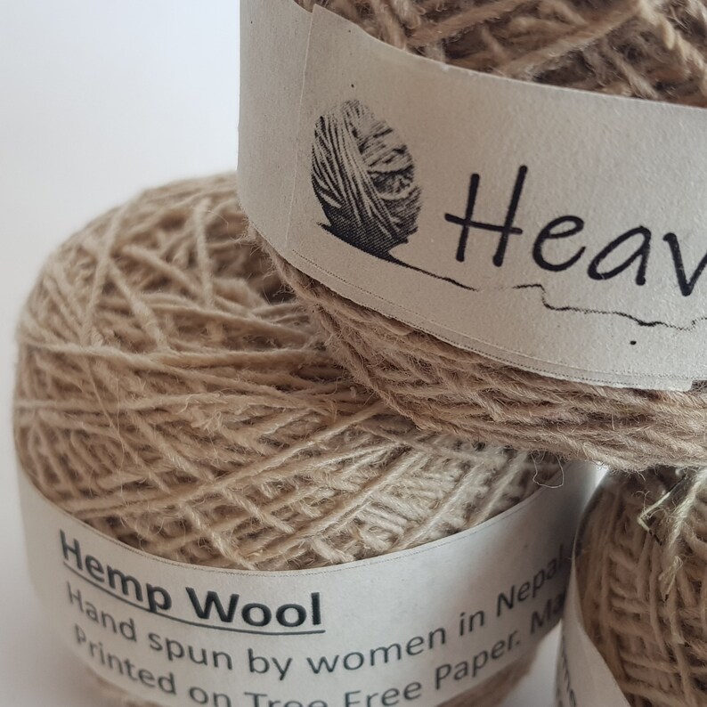 Peut inclure: Gros plan sur plusieurs pelotes de laine de chanvre. La laine est de couleur beige naturel, et les &eacute;tiquettes indiquent "Hemp Wool" et "Fil&eacute; &agrave; la main par des femmes au N&eacute;pal". Les &eacute;tiquettes pr&eacute;sentent &eacute;galement un dessin d'une pelote de laine.