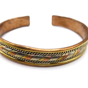 Könnte beinhalten: Ein kupferfarbenes Armband mit einem dekorativen Band aus ineinander verwobenen Metallen in Gold-, Silber- und Kupferfarben. Das Armband hat ein offenes Design und wird vor weißem Hintergrund präsentiert.