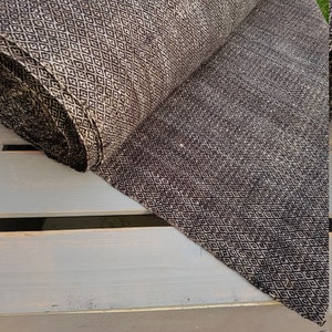 May include: A roll of fabric with a repeating diamond pattern in black and beige. The fabric is partially unrolled, revealing the pattern and texture. The fabric appears to be a medium weight, suitable for various sewing projects.