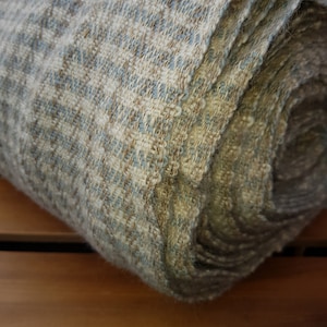 May include: Rolled-up woven fabric in shades of beige, blue, and brown. The textile has a textured appearance with a subtle pattern. The fabric is tightly woven, suggesting durability and a natural fiber composition. The roll displays the fabric's layered construction.