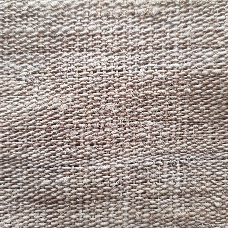 May include: Close-up of a woven fabric with a textured surface. The fabric is a neutral beige color, with a tight weave pattern. The weave creates a grid-like appearance, with visible threads and slight variations in color.
